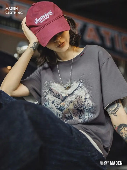 Person wearing a gray t-shirt with a graphic design and a red cap, sitting indoors.